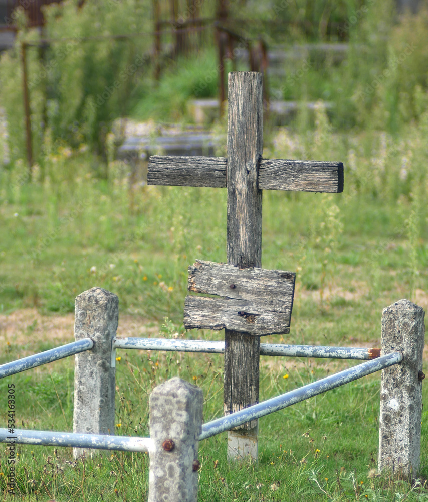 Slightly blurred wooden cross, worn out by time, on a grave, in an abandoned graveyard. Shot with vintage lens.