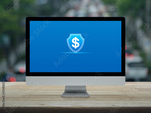 Dollar with shield flat icon on desktop modern computer monitor screen on wooden table over blur of rush hour with cars and road in city, Business money insurance and protection online concept