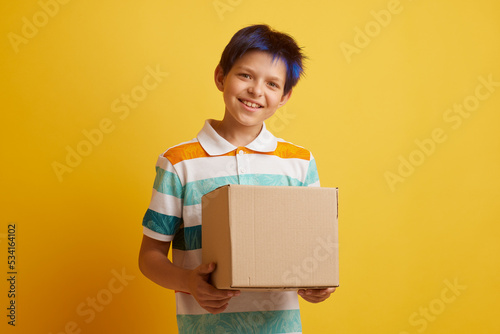 Teenage boy holding blank cardboard box over isolated yellow background, delivery concept