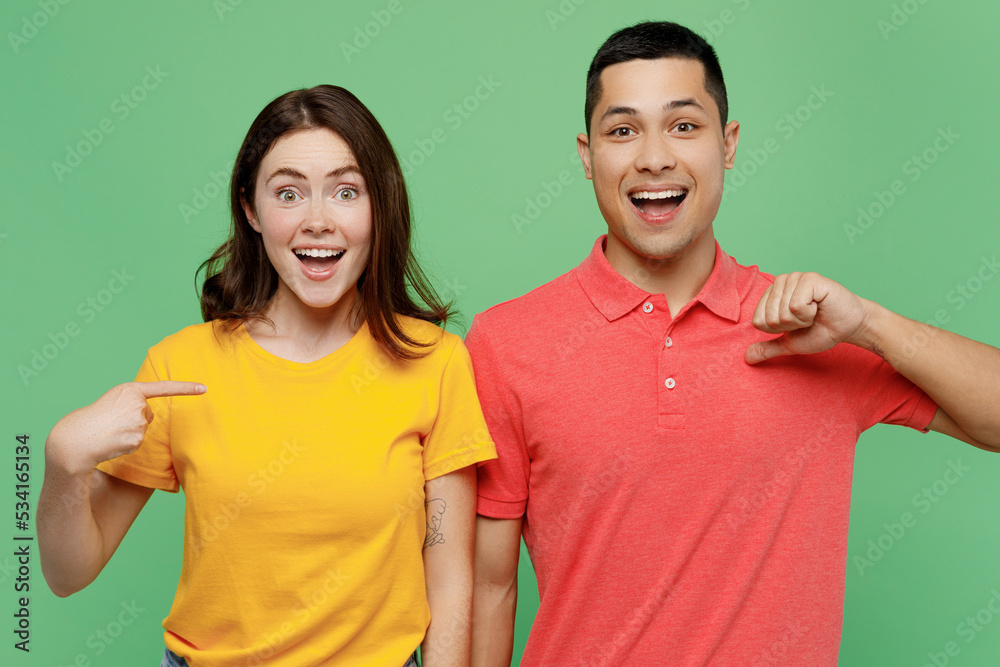 Young surprised shocked excited couple two friends family man woman wear basic t-shirts together point index finger on herself isolated on pastel plain light green color background studio portrait. Young surprised shocked excited couple two friends family man woman wear basic t-shirts together point index finger on herself isolated on pastel plain light green color background studio portrait.