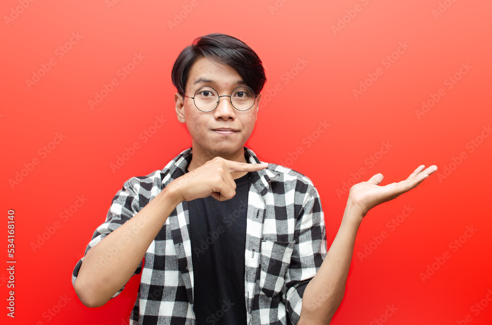 asian young man with glasses shocked happily pointing to copy space isolated over red background. billboard advertisment model concept. asian young man with glasses shocked happily pointing to copy space isolated over red background. billboard advertisment model concept.