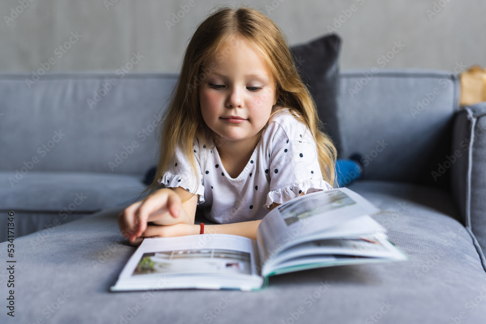 Little girl sitting on the sofa reading a book. Concept of girl with a book. Little girl sitting on the sofa reading a book. Concept of girl with a book.