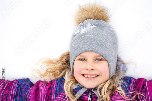 The child girl lay down on the snow and smiles.