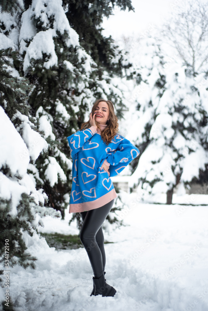 girl is standing in a blue sweater near the Christmas tree, it's snowing