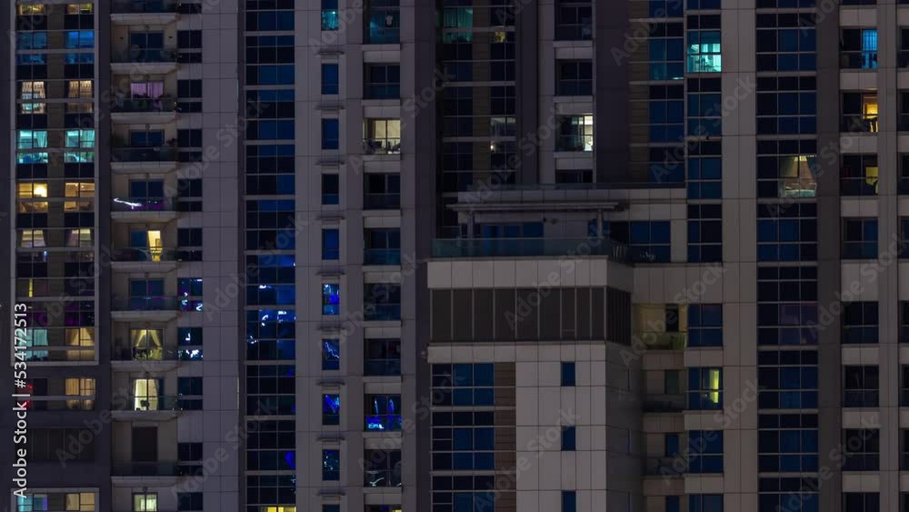 Apartment windows of a glazed skyscraper glow at night with city lights reflection aerial timelapse. Illuminated towers with blue light Apartment windows of a glazed skyscraper glow at night with city lights reflection aerial timelapse. Illuminated towers with blue light