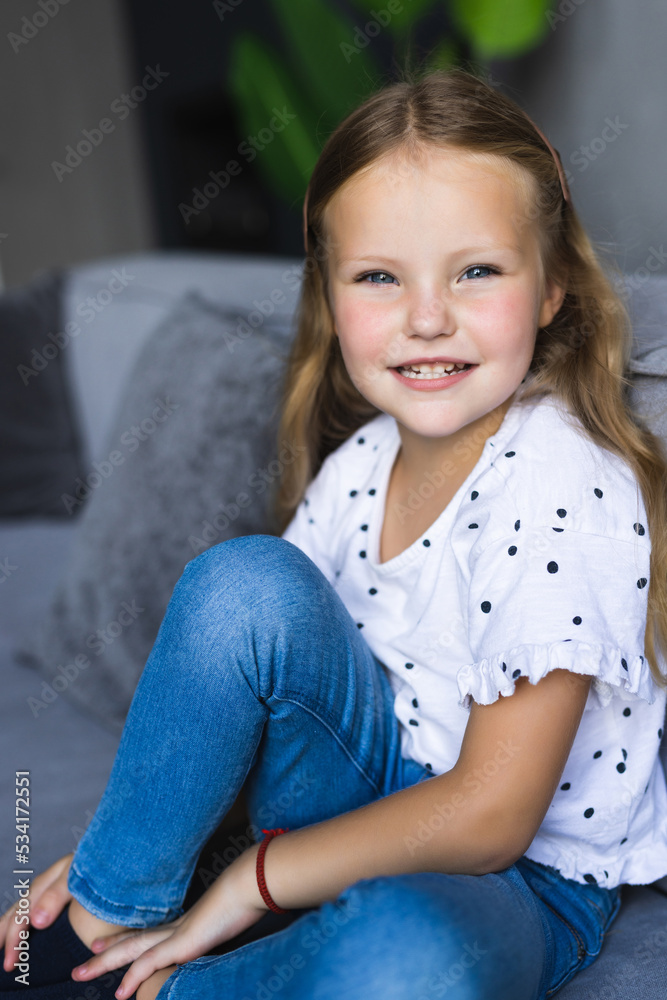 Pretty happy little girl in casual wearing sitting on sofa Pretty happy little girl in casual wearing sitting on sofa