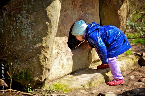 Girl looks out of the narrow passage of the cave. Exploring wild places and attractions in nature.