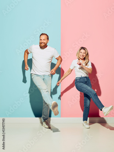 Dance. Studio shot of couple of young funny and happy man and woman having fun isolated over blue and pink background.