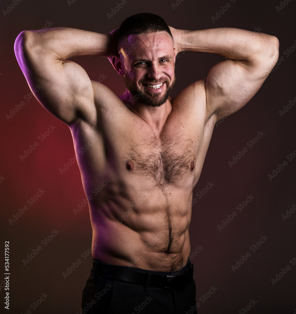 Portrait of a handsome muscular bodybuilder posing over warm dark background. Naked muscular torso, chest, biceps and abs