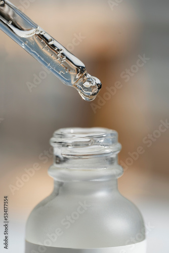 Open transparent bottle with dropper pipette with serum or essential oil. Medicine and beauty concept for face care. Selective focus in the center