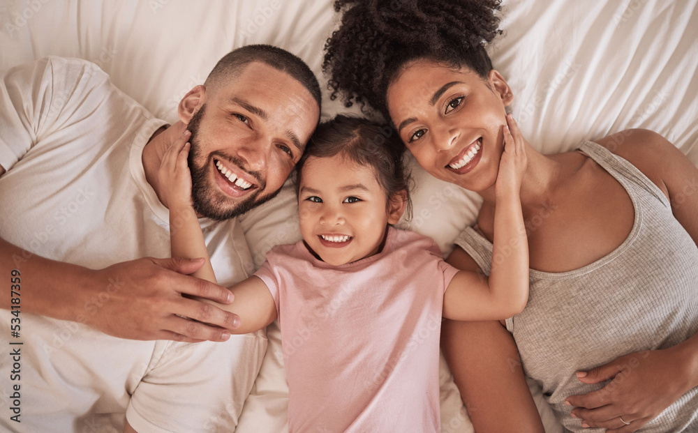 Family happy, child and above bed with parents in the morning, funny face in house and relax after sleeping together in home. Portrait of happy mother and dad smile with girl kids in home bedroom