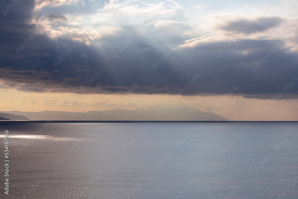 Early morning view of the sunrise over the Mediterranean Aegean Sea. View on the peninsula Mount Athos (Again Oros), Chalkidiki, Central Macedonia, Greece, Europe. Sun beams on the water surface, calm