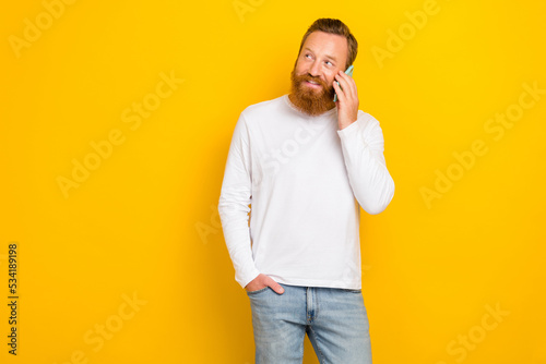 Portrait photo of young redhair man solid worker influencer talking phone user look empty space advert isolated on yellow color background photo