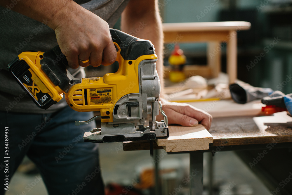 A wood-worker using a jigsaw to cut out a curve in a work piece of pine.