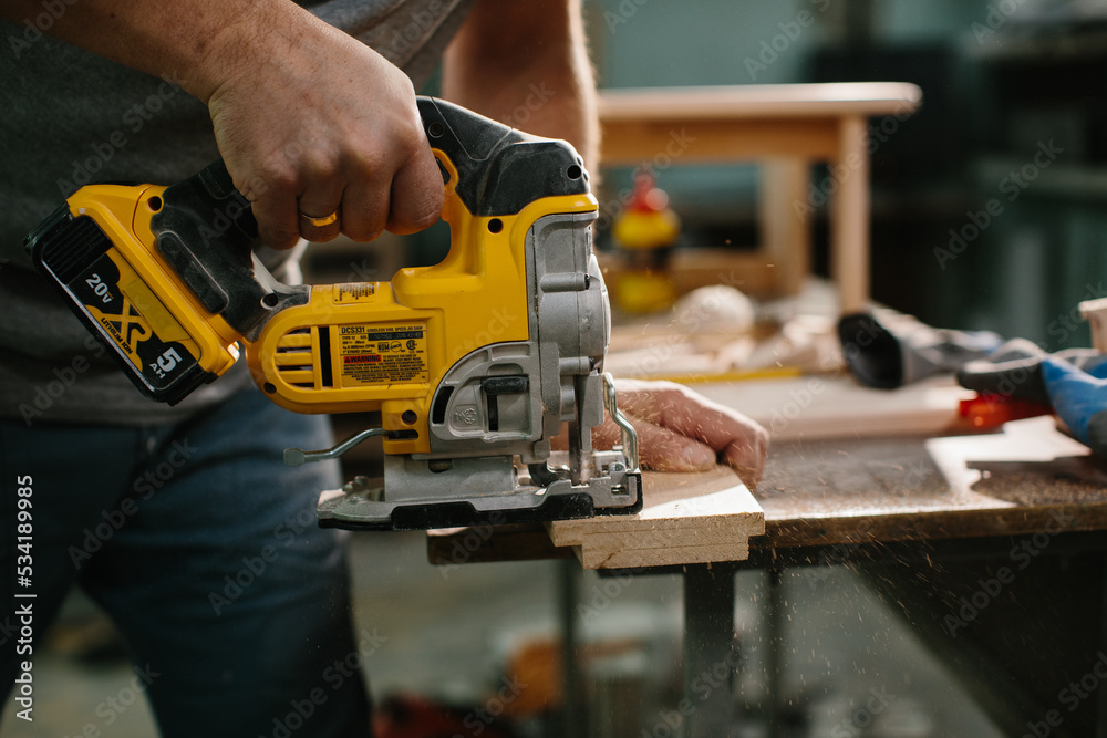 Close up on hand of unknown carpenter working with an electric jigsaw cutting wood with saw. Close up on hand of unknown carpenter working with an electric jigsaw cutting wood with saw.