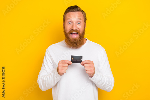 Photo of positive satisfied glad man stylish sweater outfit arm hold credit card impressed reaction isolated on yellow color background