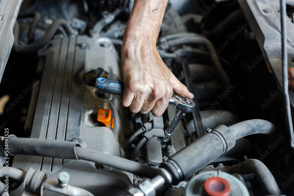 An auto mechanic works with a car engine in the mechanics' garage. Car repair close-up. An authentic close-up shot of an auto mechanic's hands. An auto mechanic works with a car engine in the mechanics' garage. Car repair close-up. An authentic close-up shot of an auto mechanic's hands.