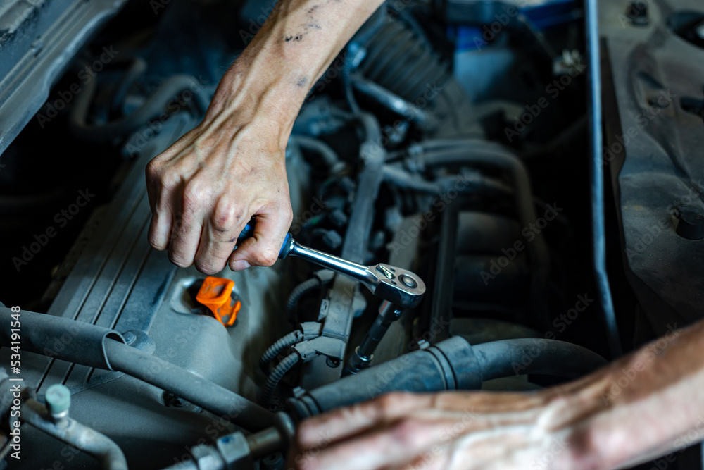 An auto mechanic works with a car engine in the mechanics' garage. Car repair close-up. An authentic close-up shot of an auto mechanic's hands. An auto mechanic works with a car engine in the mechanics' garage. Car repair close-up. An authentic close-up shot of an auto mechanic's hands.