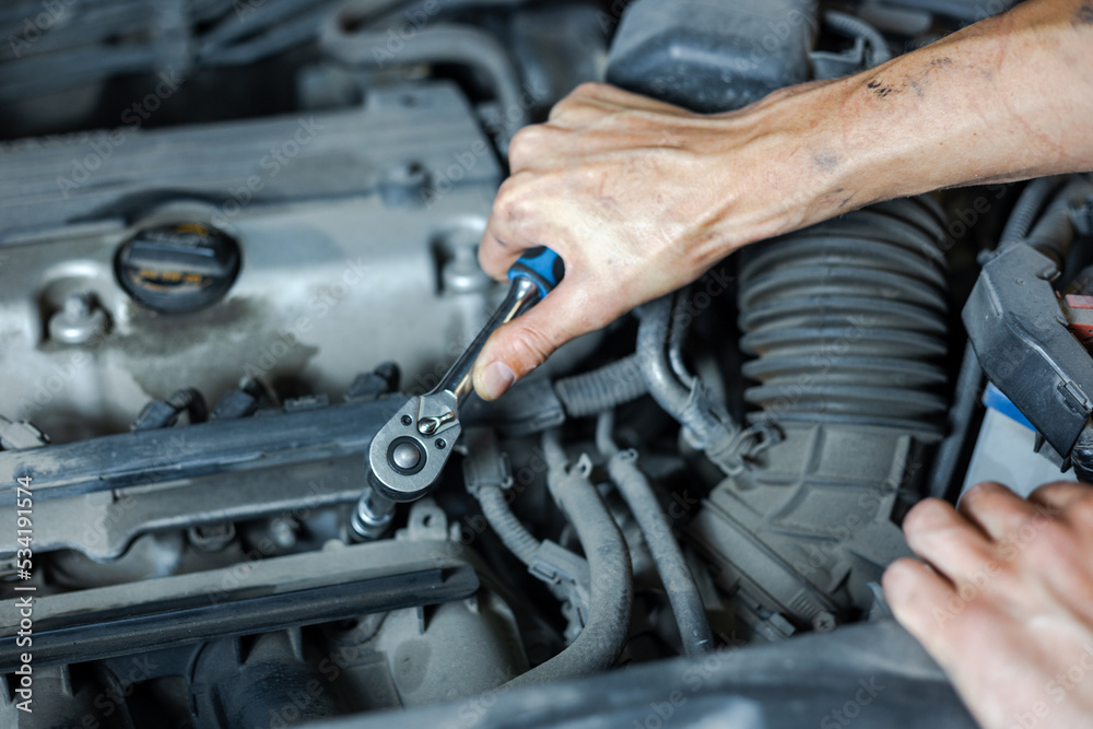 Fototapeta premium An auto mechanic works with a car engine in the mechanics' garage. Car repair close-up. An authentic close-up shot of an auto mechanic's hands.