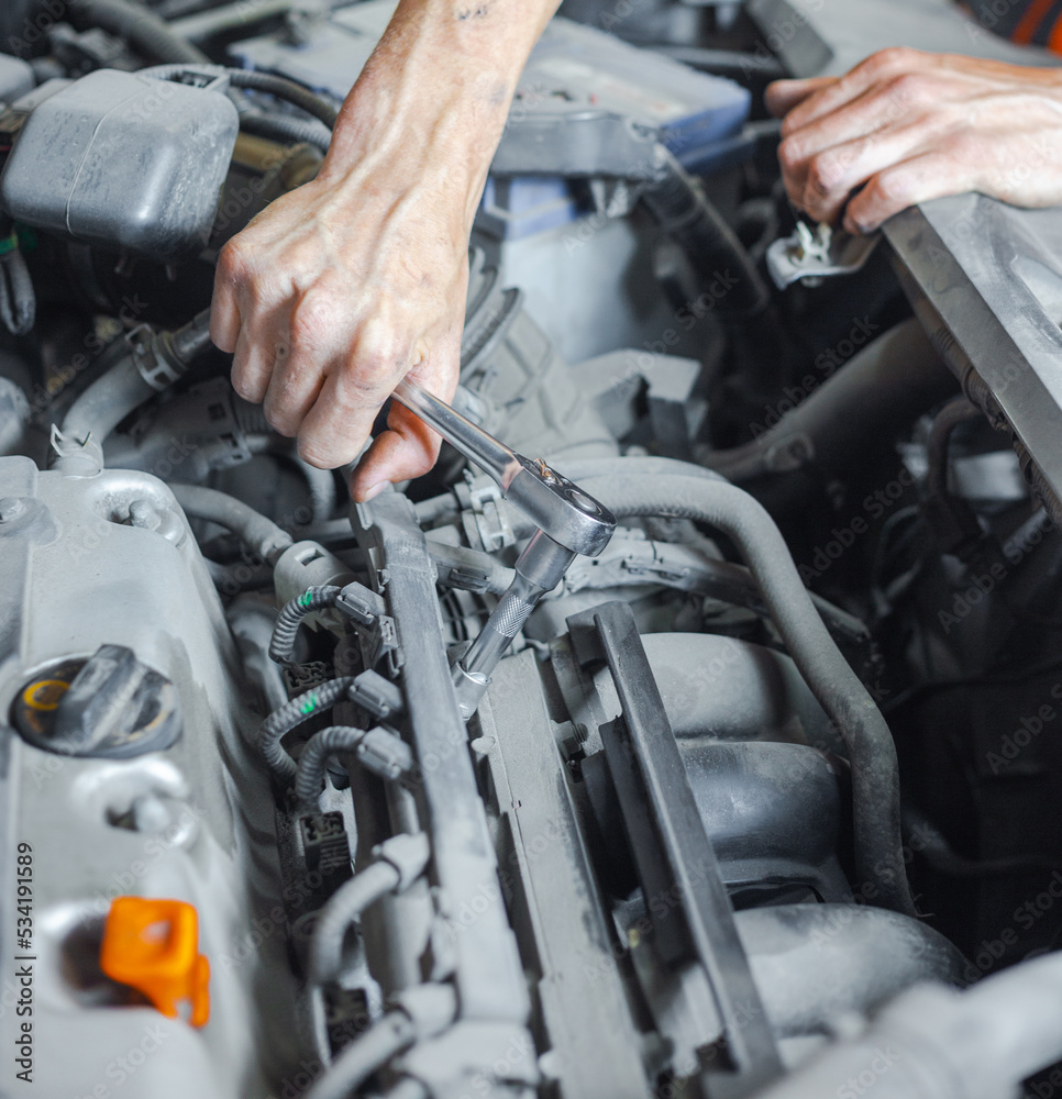 An auto mechanic works with a car engine in the mechanics' garage. Car repair close-up. An authentic close-up shot of an auto mechanic's hands. An auto mechanic works with a car engine in the mechanics' garage. Car repair close-up. An authentic close-up shot of an auto mechanic's hands.