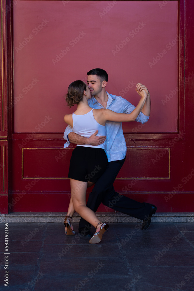 Boy in a suit and girl in shorts and a white t-shirt Couple dancing Tango, with a red background.