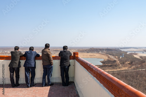 FANGCHUAN TRIPOINT, JILIN : Chinese men watching Russian territory and the bridge across the Tumen river, into North Korea