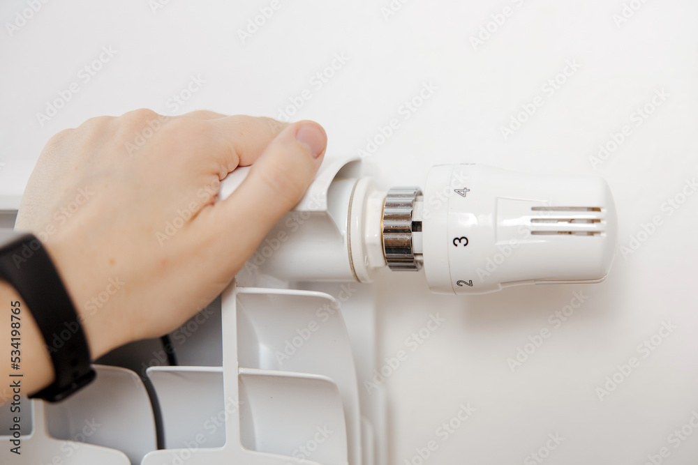 Woman hand on white heating radiator, close up view. It is cold, person warms up. Central heating system. Heating is getting more expensive, save money. Energy crisis. Woman hand on white heating radiator, close up view. It is cold, person warms up. Central heating system. Heating is getting more expensive, save money. Energy crisis.