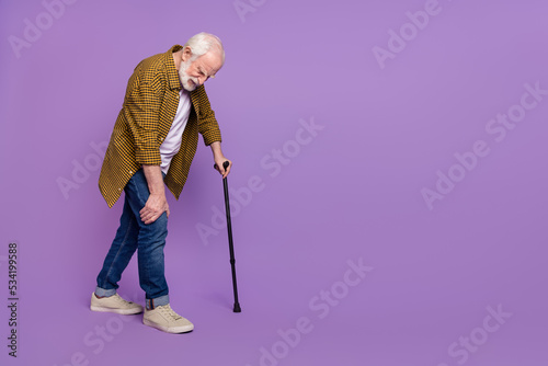 Full body photo of sad granddad grey hair touch sick leg cane wear stylish yellow checkered shirt isolated on lilac purple color background