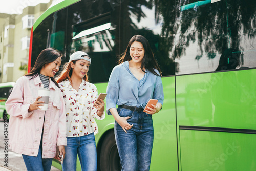 Canvas Print Happy young asian friends using mobile phones at bus station - Focus on center g