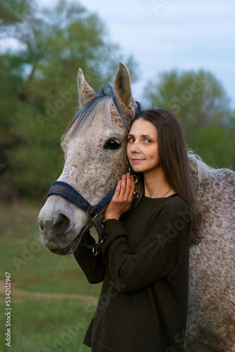Girl hugging a fleabitten grey horse and looking at the camera
