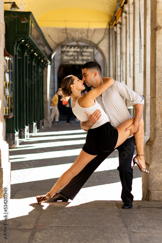 Couple dancing Tango. Boy in a suit and girl in shorts and a white t-shirt, between stone arches. Tango position.