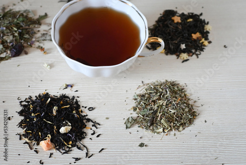 A set of different types tea next to the kettle filled with hot brewed tea on a beige background.