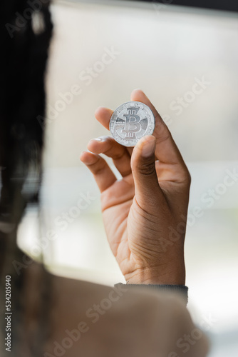 KYIV, UKRAINE - APRIL 27, 2022: Blurred african american businesswoman holding silver bitcoin in office.