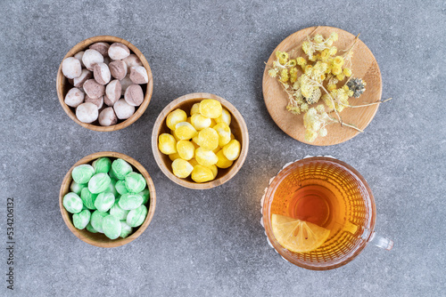 Bowls of colorful candies with hot tea on marble background