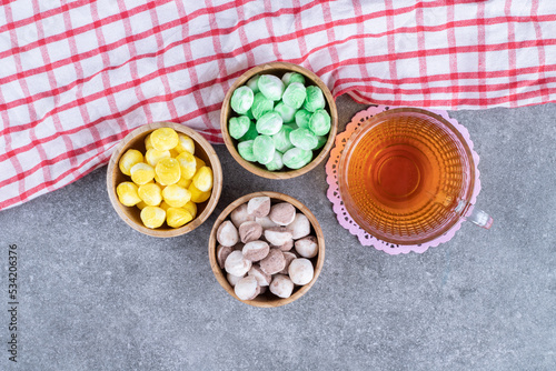 Three bowls of colorful candies with hot tea on marble background