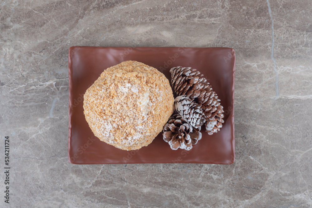 Pine cones and a squirrel cake on a brown platter on marble background