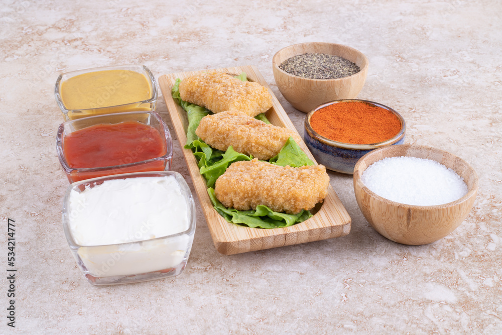 Chicken nuggets on a wooden board with variety of sauces around