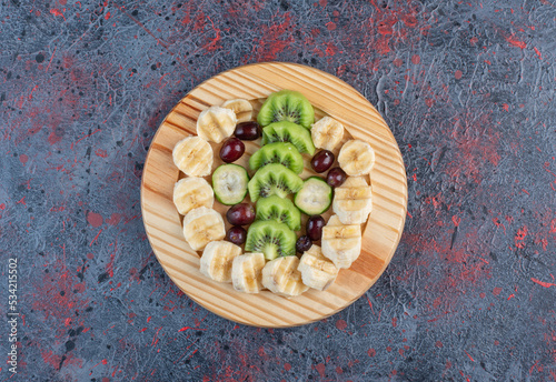 Fruit salad with sliced banana, kiwies and berries in a wooden plate photo