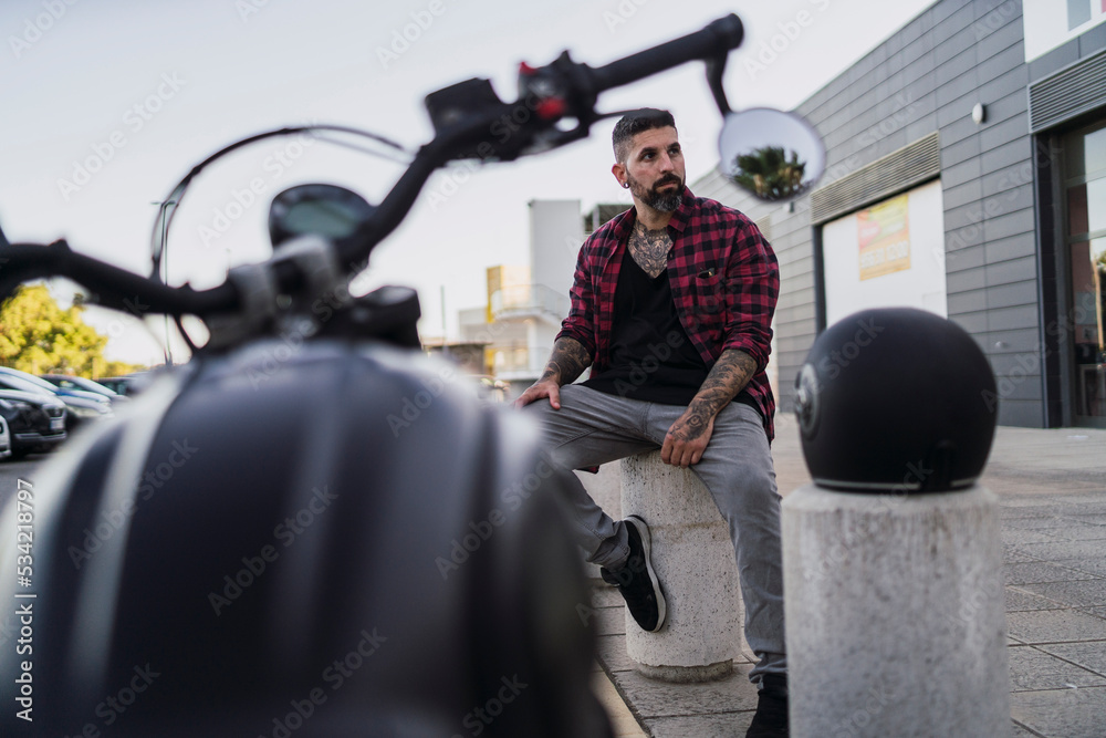 Chico con camisa a cuadros roja posando con su casco de moto y la motocicleta