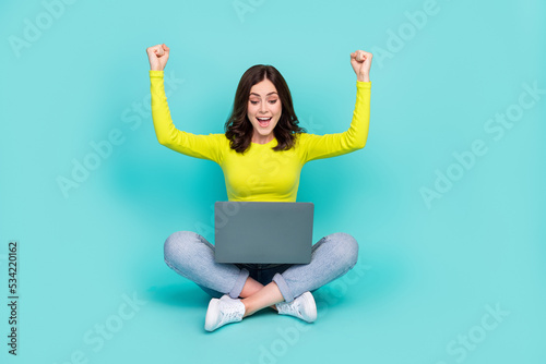 Full length photo of delighted person sit floor use netbook raise fists success isolated on aquamarine color background © deagreez