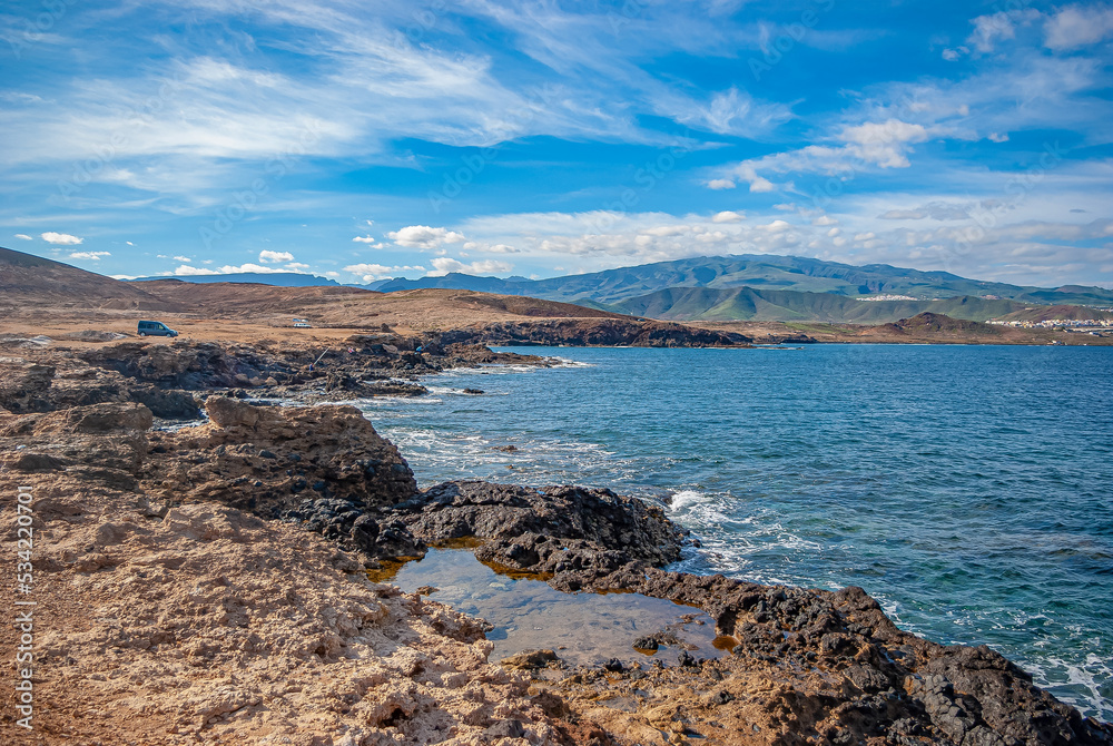 Scenic view of volcanic black sand beach, Canary Islands, Spain, Europe. Mountains in the distance. Sky with white clouds. Scenic view of volcanic black sand beach, Canary Islands, Spain, Europe. Mountains in the distance. Sky with white clouds.