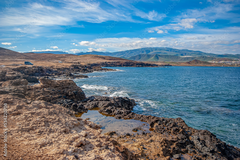 Scenic view of volcanic black sand beach, Canary Islands, Spain, Europe. Mountains in the distance. Sky with white clouds.