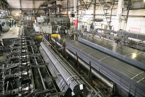 Plant for the production of metal pipes. Workshop with mechanical tools and equipment, rolls of steel for the production of metal pipes. Stack of steel pipes.