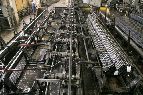 Plant for the production of metal pipes. Workshop with mechanical tools and equipment, rolls of steel for the production of metal pipes. Stack of steel pipes.
