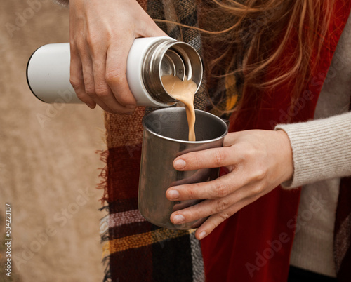 A woman pours coffee with milk into a cup from a thermos. Tourism and travel. Autumn photos. photo