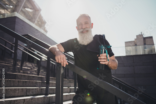 Portrait of attractive cheerful healthy grey-haired man spending good day drinking water active time downtown outdoors