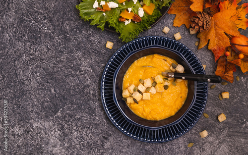 Bowl of pumpkin soup with croutons and seeds on stone kitchen counter. Copy space for your text