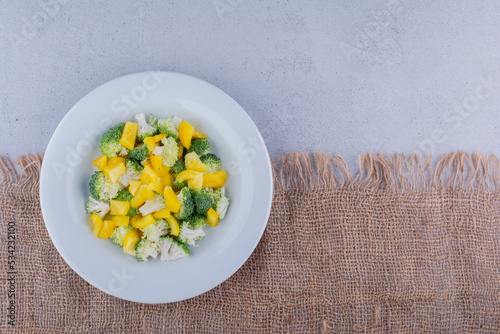 Chopped broccoli, cauliflower and yellow bell pepper mixed into a salad on marble background