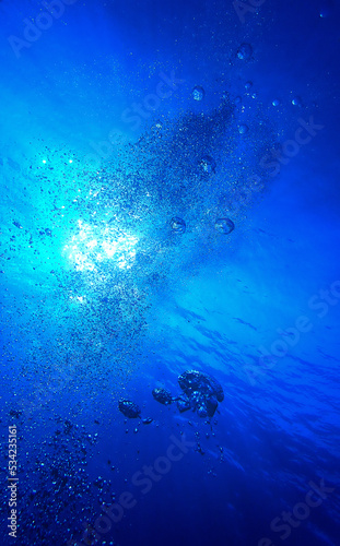 Air bubbles going up against the surface underwater in rays of sunlight