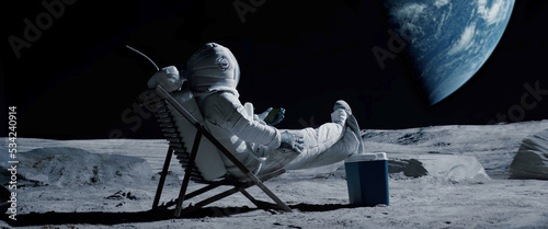 Astronaut sits in a beach chair on a Moon surface, holding phone in hands photo